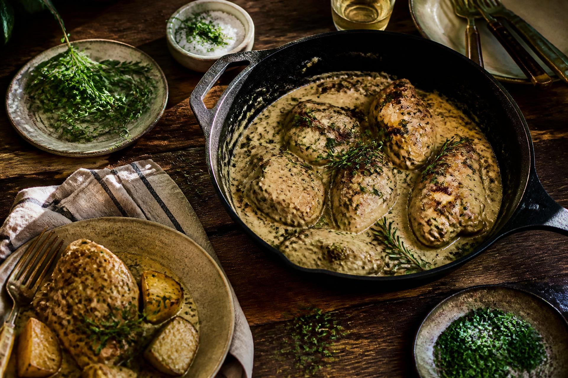 Creamy herb chicken in a cast iron pan on a rustic wooden table with fresh herbs